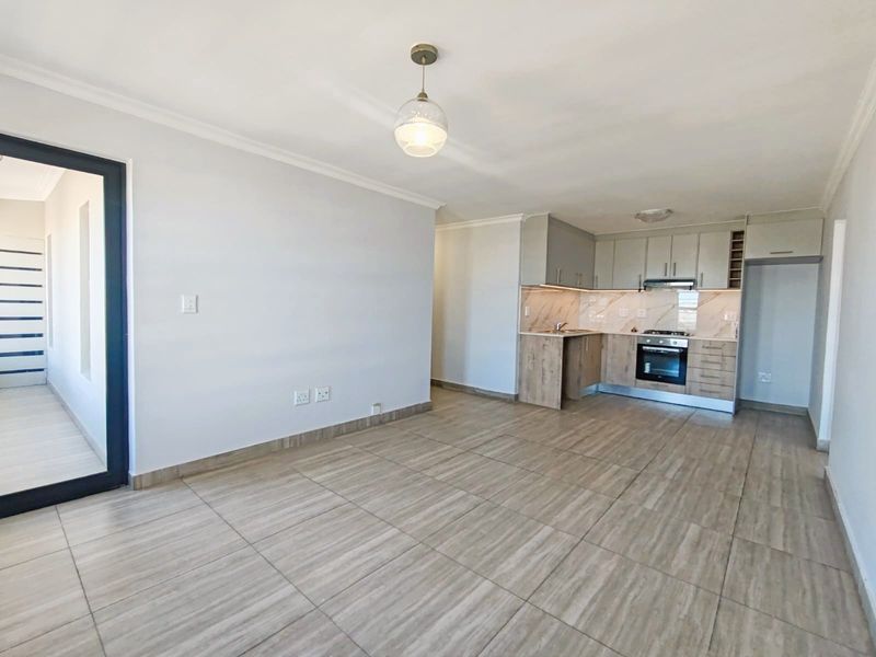 An open-plan living and kitchen area featuring modern cabinetry, built-in appliances, tiled flooring, and neutral finishes, providing a clean and versatile space.