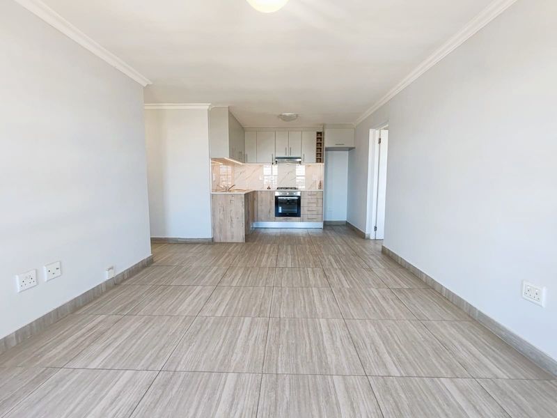 An open-plan living and kitchen area featuring modern wood-finish cabinetry, integrated appliances, and neutral tiled flooring throughout.