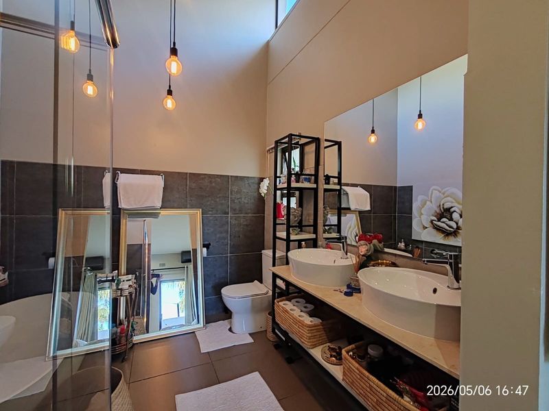 Modern bathroom featuring a double vanity with vessel sinks, large wall mirror, glass shower enclosure, and contemporary tiled finishes.