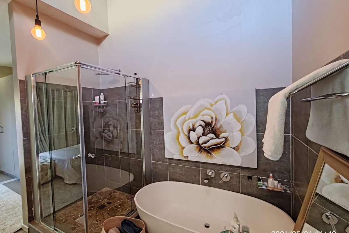 Modern bathroom featuring a freestanding bathtub, glass-enclosed shower, and contemporary tiled finishes with high ceilings and pendant lighting.
