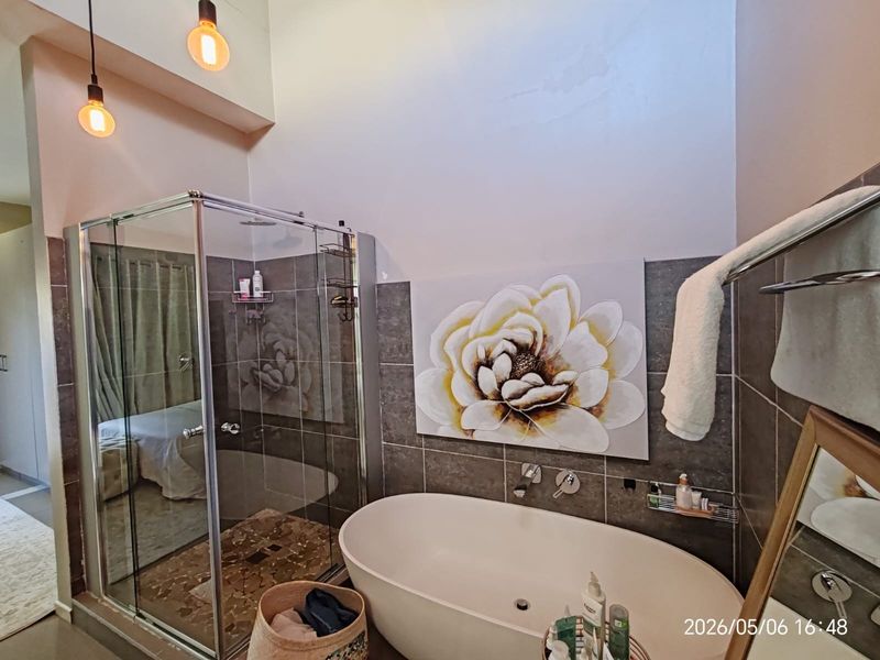 Modern bathroom featuring a freestanding bathtub, glass-enclosed shower, and contemporary tiled finishes with high ceilings and pendant lighting.