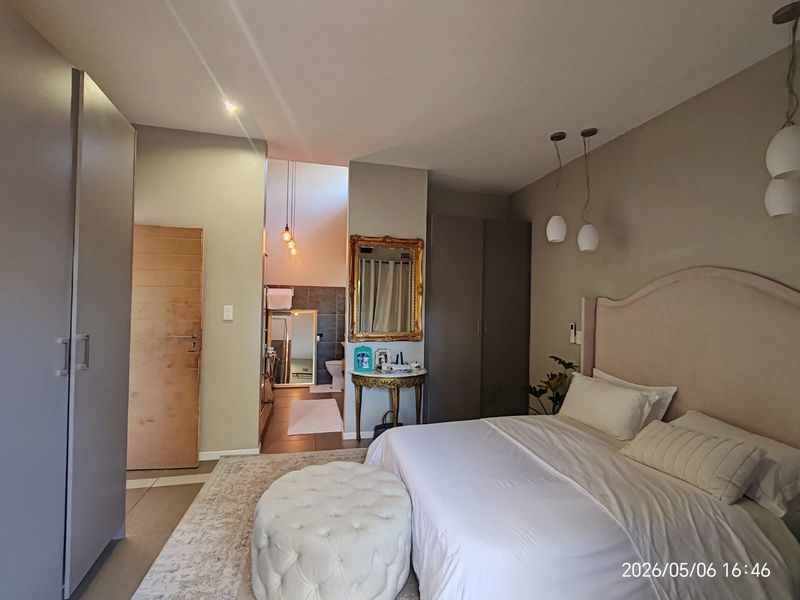 Spacious bedroom featuring built-in cupboards, neutral finishes, and an open-plan en-suite bathroom with modern lighting.