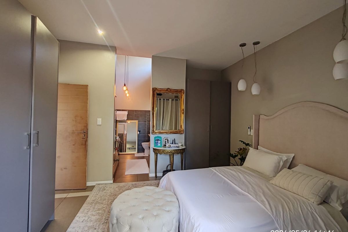 Spacious bedroom featuring built-in cupboards, neutral finishes, and an open-plan en-suite bathroom with modern lighting.