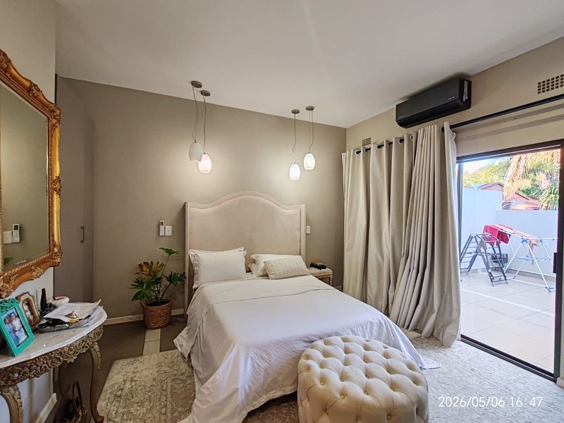 A well-maintained bedroom featuring pendant lighting, a split-system air conditioner, and direct access to an outdoor patio through a sliding glass door.