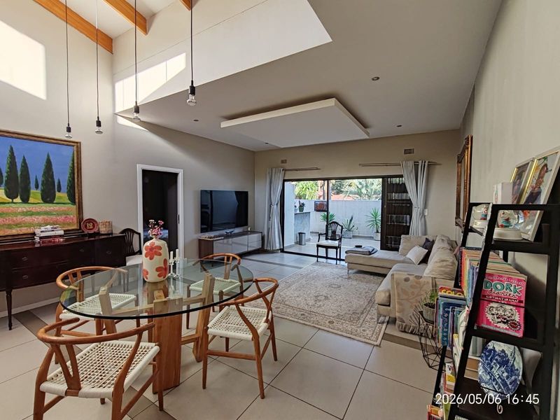 Spacious open-plan living and dining area featuring high vaulted ceilings with exposed timber beams, tiled flooring, and large sliding doors leading to a patio.