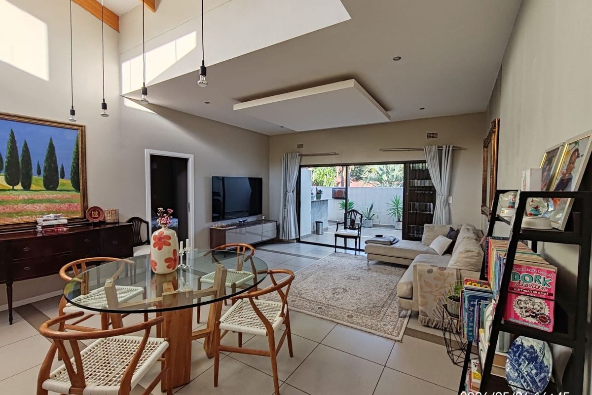 Spacious open-plan living and dining area featuring high vaulted ceilings with exposed timber beams, tiled flooring, and large sliding doors leading to a patio.