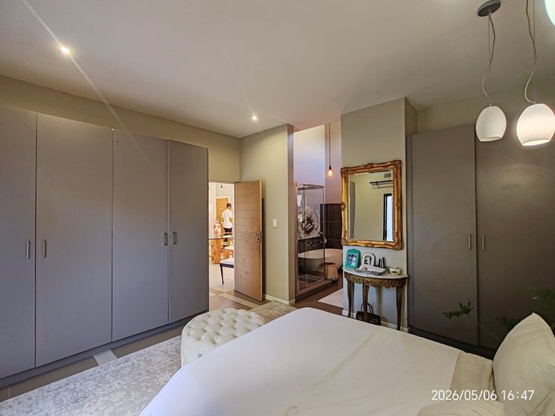 Spacious bedroom featuring extensive built-in cupboards, recessed lighting, and direct access to an en-suite bathroom with a modern layout.