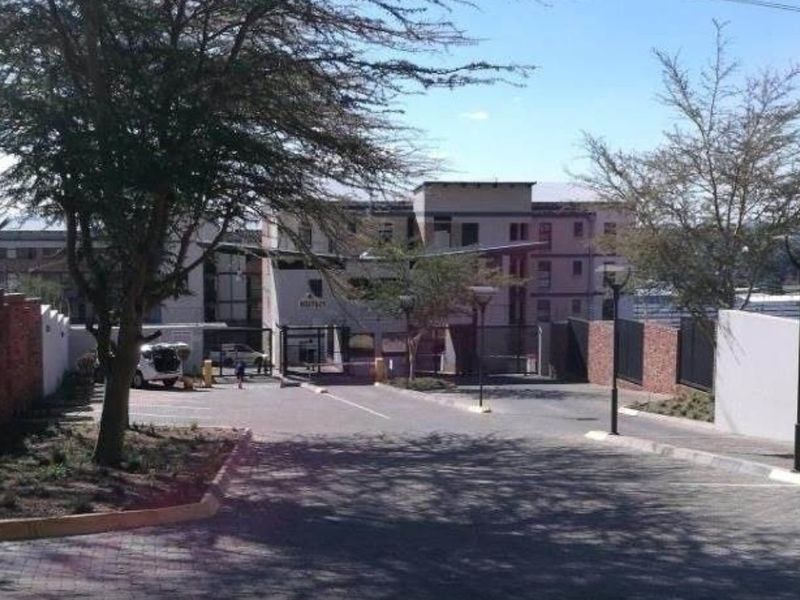 View of the apartment complex entrance featuring a paved driveway, secure gated access, and perimeter walling.