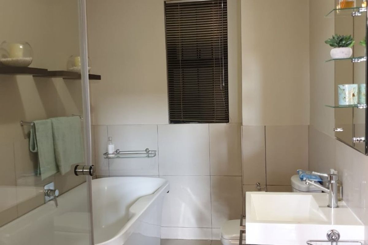 A well-maintained bathroom featuring a freestanding bathtub, glass shower screen, modern vanity with basin, and neutral wall and floor tiling.