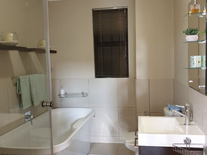 A well-maintained bathroom featuring a freestanding bathtub, glass shower screen, modern vanity with basin, and neutral wall and floor tiling.