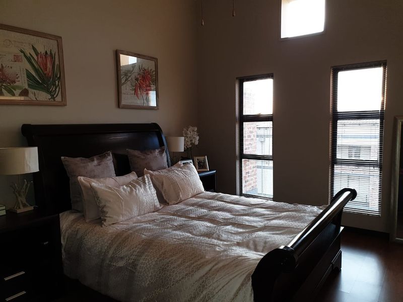 A well-maintained bedroom featuring laminate flooring, tall vertical windows with venetian blinds, and a high-level clerestory window providing natural light.
