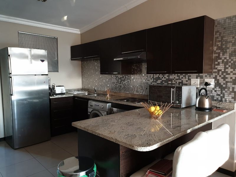 Modern kitchen featuring dark cabinetry, granite countertops, mosaic tile backsplash, and integrated appliances, offering a functional and stylish cooking space.