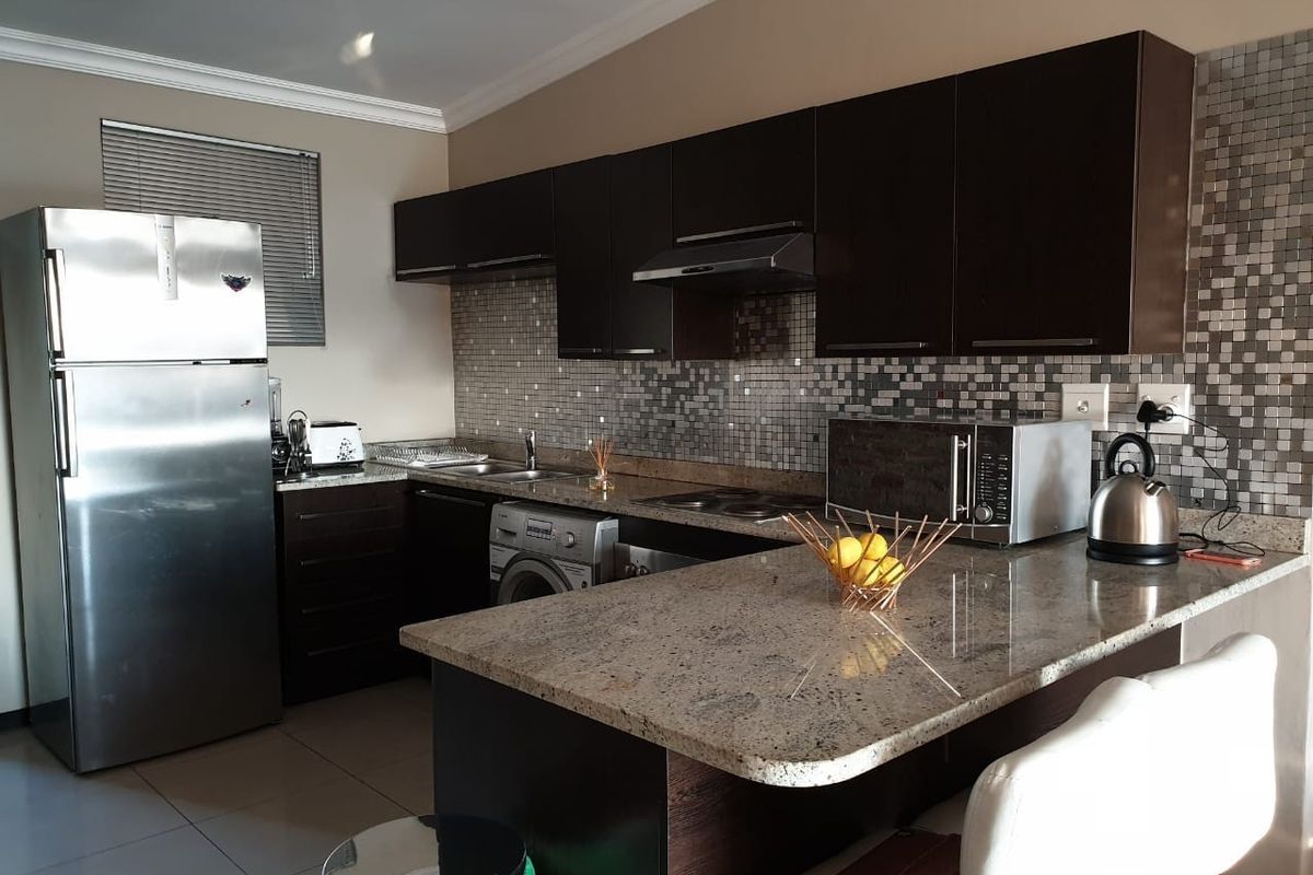 Modern kitchen featuring dark cabinetry, granite countertops, mosaic tile backsplash, and integrated appliances, offering a functional and stylish cooking space.