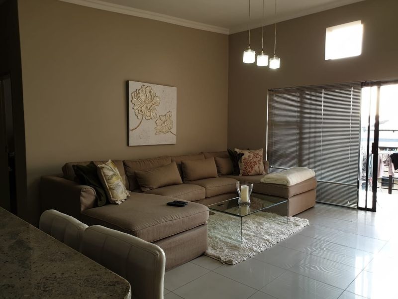 A well-maintained living room featuring tiled floors, modern pendant lighting, and a sliding glass door leading to an outdoor area with venetian blinds.