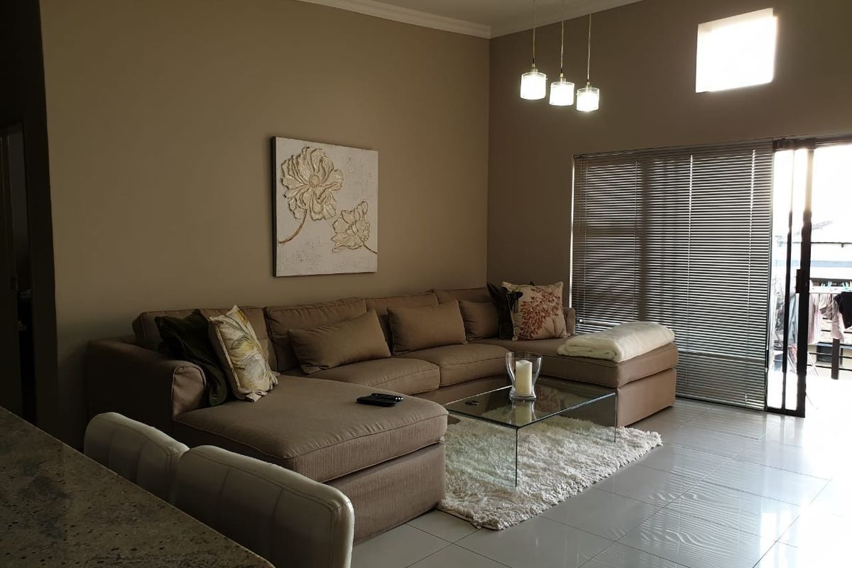 A well-maintained living room featuring tiled floors, modern pendant lighting, and a sliding glass door leading to an outdoor area with venetian blinds.