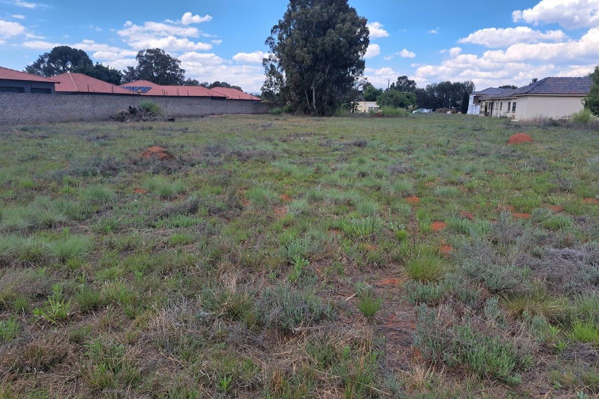 A vacant residential plot featuring natural grass cover, mature trees, and enclosed by perimeter boundary walls in a established neighborhood.