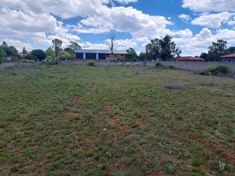 A vacant residential plot featuring natural grassland and a perimeter boundary wall, offering a clear space for future development.