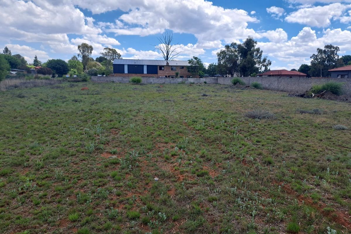 A vacant residential plot featuring natural grassland and a perimeter boundary wall, offering a clear space for future development.