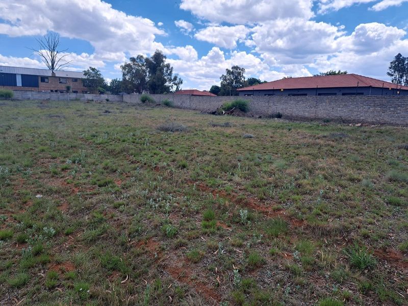 A vacant residential plot featuring a level grass surface enclosed by a perimeter brick wall with installed electric fencing.