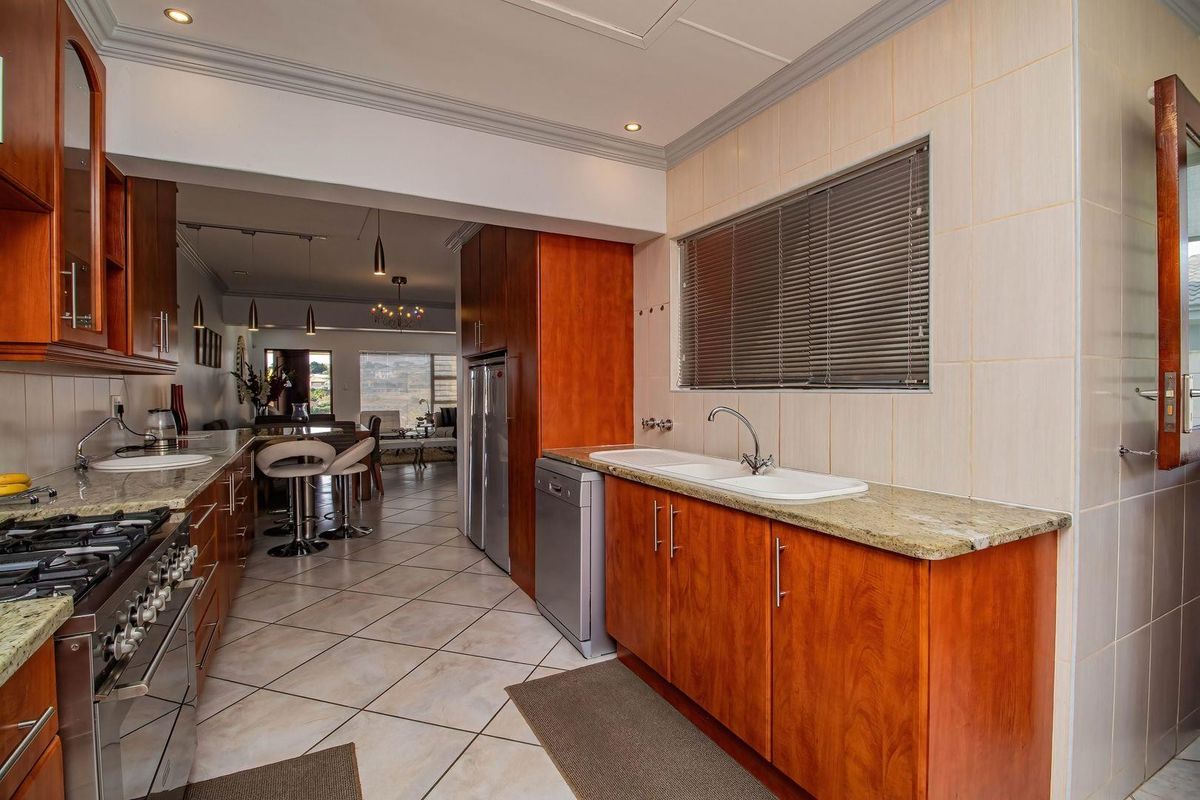A functional kitchen featuring warm-toned wooden cabinetry, granite countertops, a gas stove, and a double basin sink, flowing into an open-plan living area.