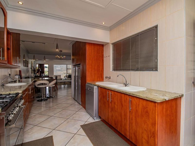 A functional kitchen featuring warm-toned wooden cabinetry, granite countertops, a gas stove, and a double basin sink, flowing into an open-plan living area.