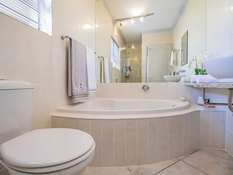 A well-maintained bathroom featuring a built-in corner bathtub, a modern vessel sink on a granite vanity, and neutral wall tiling.