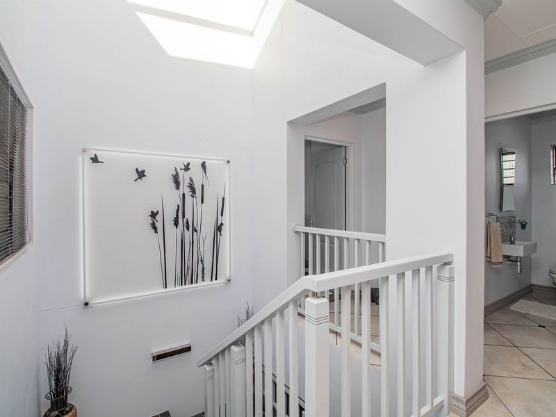 Bright upper-level hallway featuring a skylight, white balustrade, and tiled flooring, providing access to adjacent rooms.