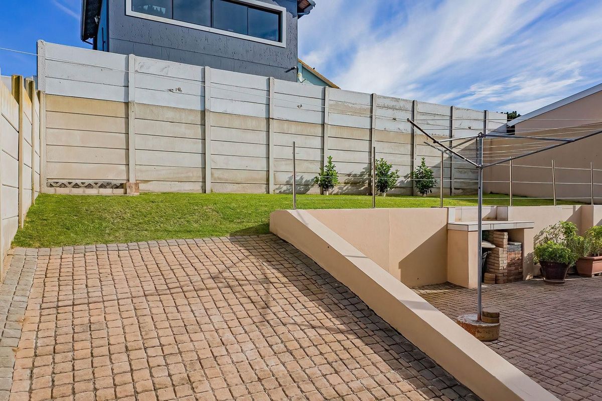 Rear exterior area featuring a paved driveway, a built-in braai, a retaining wall, and a lawn enclosed by a precast concrete boundary wall.