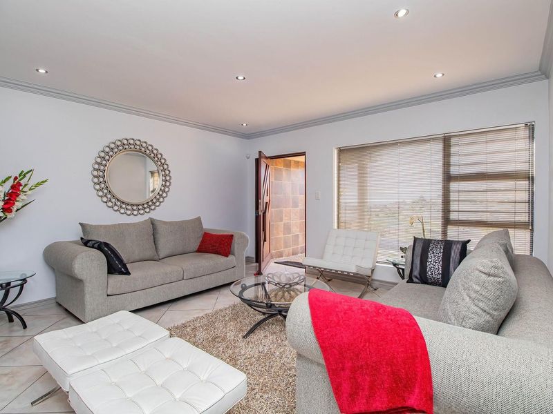 A well-maintained living room featuring tiled flooring, recessed downlights, decorative cornicing, and large windows with venetian blinds, providing a bright and comfortable living space.