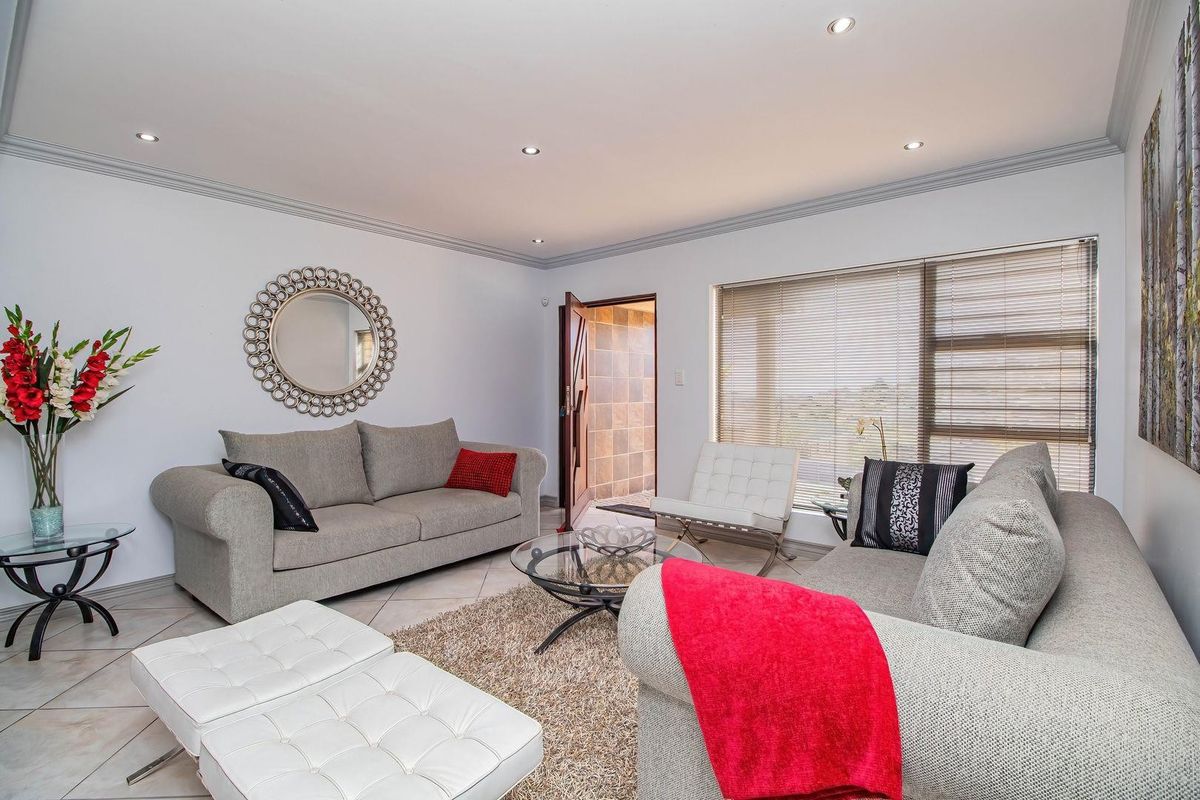 A well-maintained living room featuring tiled flooring, recessed downlights, decorative cornicing, and large windows with venetian blinds, providing a bright and comfortable living space.