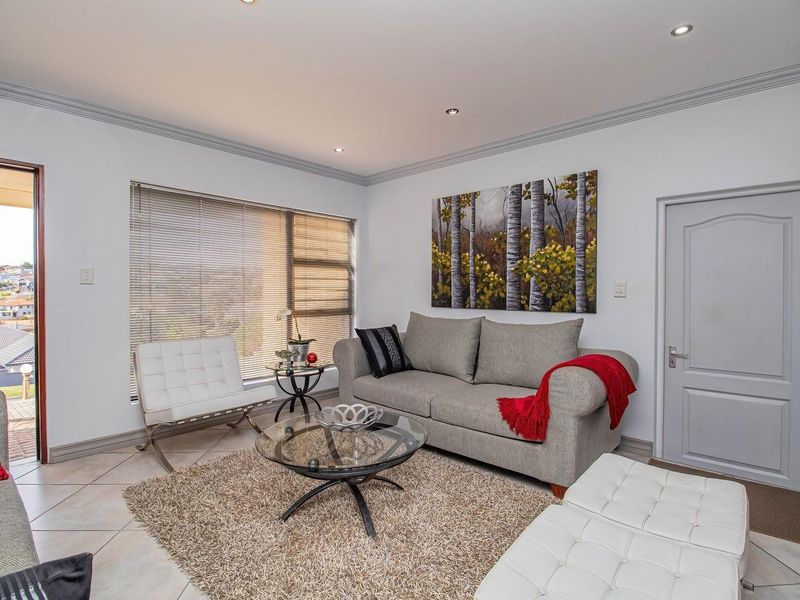 A well-maintained living room featuring tiled flooring, recessed downlighting, crown molding, and large windows with horizontal blinds, offering a bright and comfortable living space.