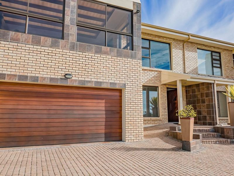 Modern duet property featuring a brick facade with tiled accents, a timber double garage door, and a paved driveway leading to a covered entrance.