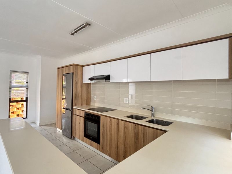 Modern kitchen featuring sleek wood-grain and white cabinetry, stone countertops, integrated appliances, and a double basin sink with a neutral tiled backsplash.