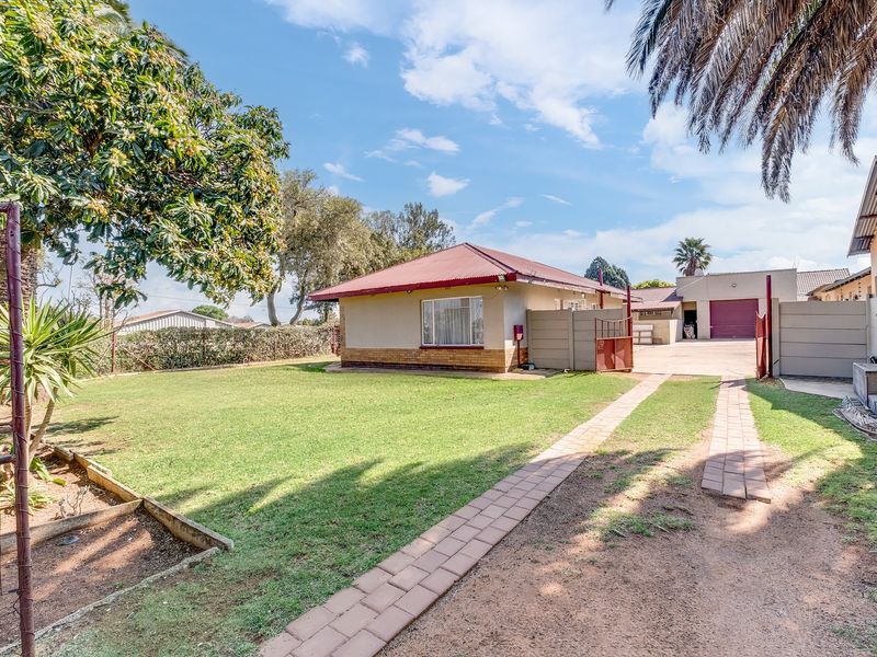 Rear view of the property featuring a spacious lawn, paved driveway, and a detached garage with a metal door.