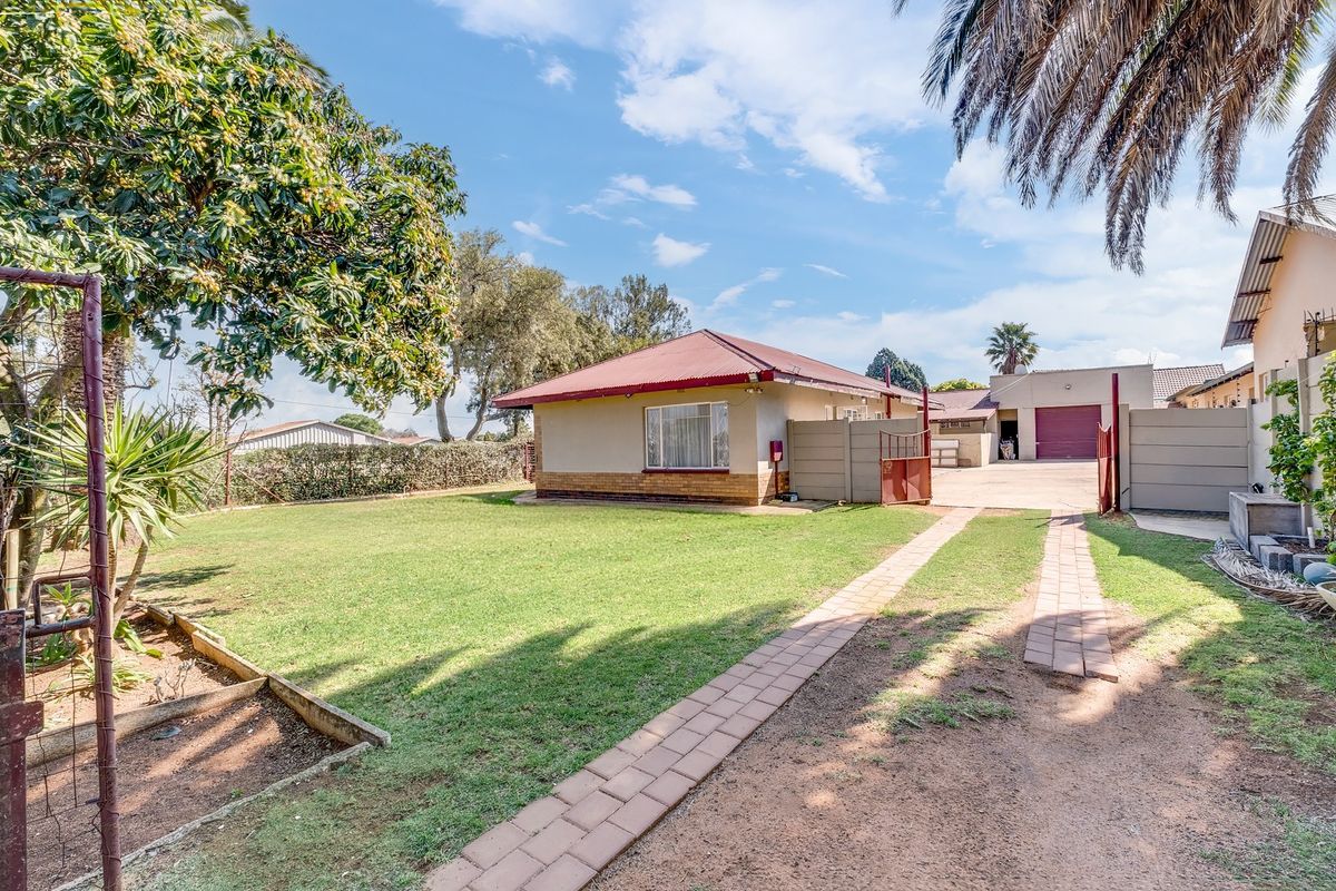 Rear view of the property featuring a spacious lawn, paved driveway, and a detached garage with a metal door.
