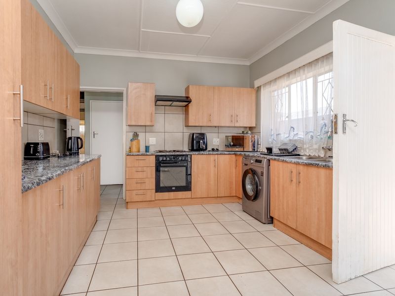 Functional kitchen featuring light wood-finish cabinetry, granite countertops, tiled flooring, and integrated appliances, offering a practical layout with ample storage space.