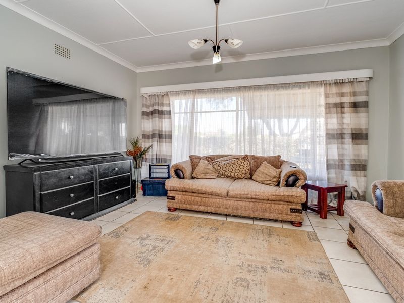 A well-lit living room featuring neutral tiled flooring, classic ceiling cornicing, and a large window with natural light.
