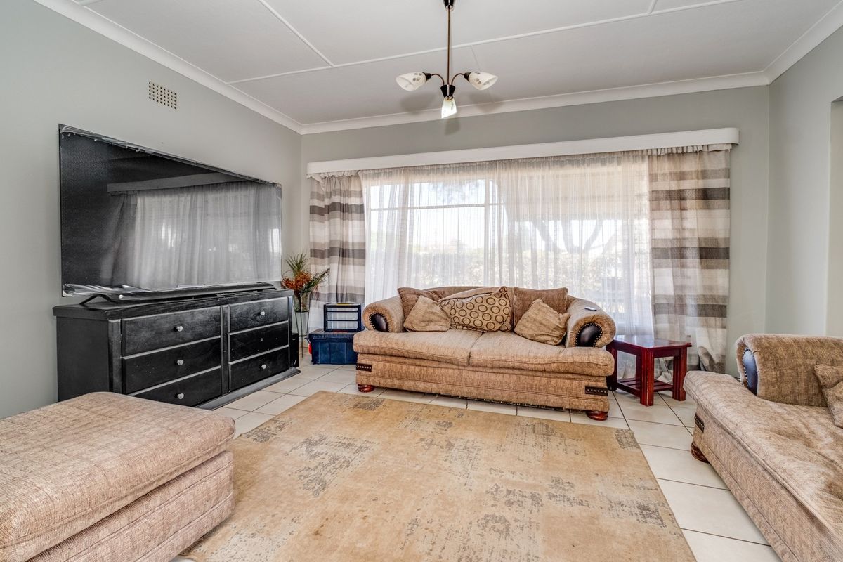 A well-lit living room featuring neutral tiled flooring, classic ceiling cornicing, and a large window with natural light.