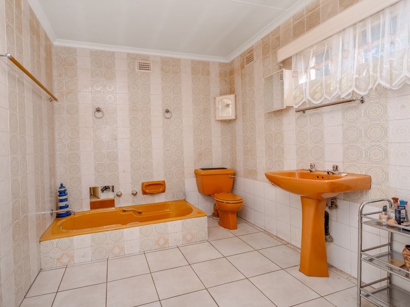 A spacious bathroom featuring vintage orange sanitaryware, including a built-in bathtub, pedestal basin, and toilet, complemented by patterned wall tiles and floor tiling.
