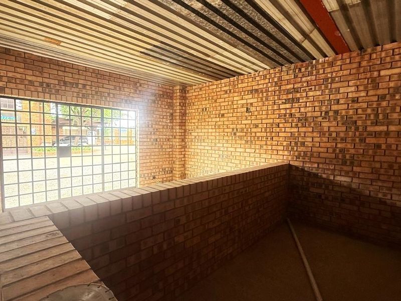 An unfinished industrial utility space featuring exposed brick walls, a corrugated metal ceiling, and a secure metal entrance gate.