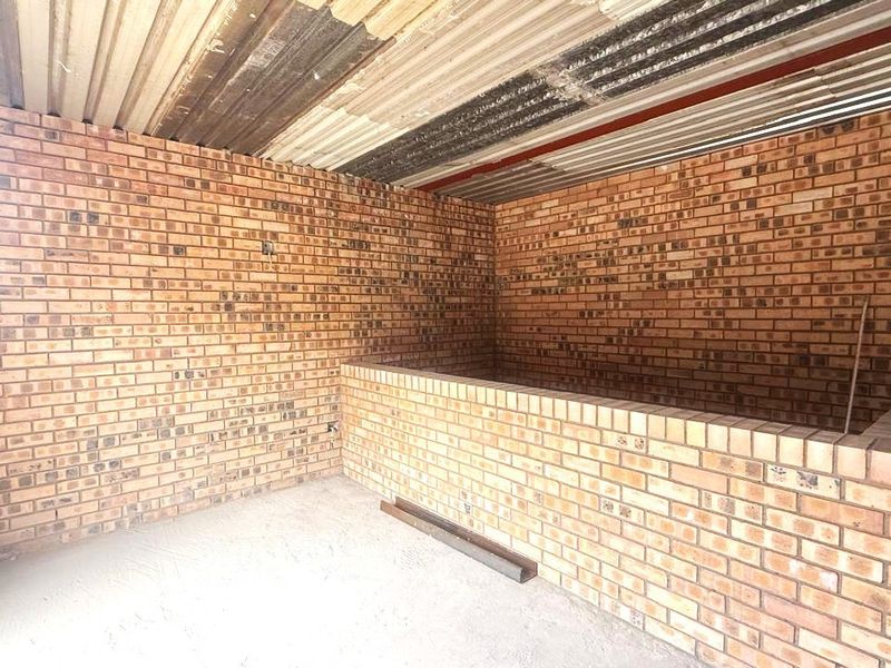 An unfinished industrial utility space featuring exposed brick walls, a corrugated metal roof, and a central brick partition wall.