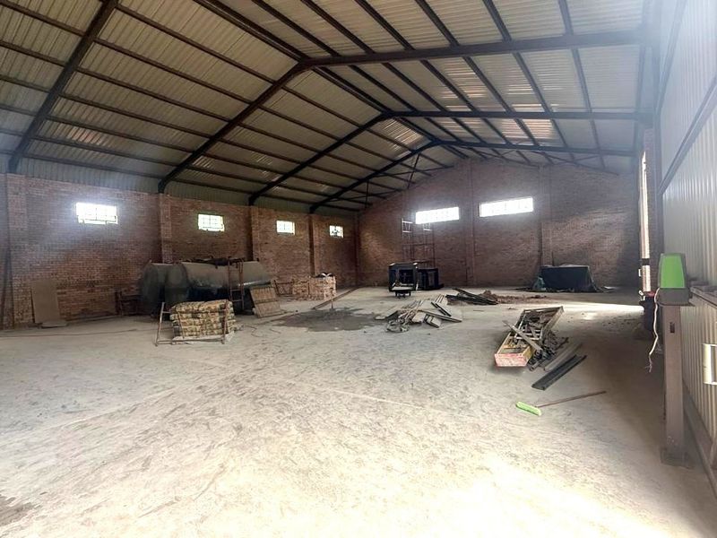 Spacious industrial utility space featuring exposed brick walls, concrete flooring, and high-clearance steel roof trusses, suitable for storage or workshop operations.