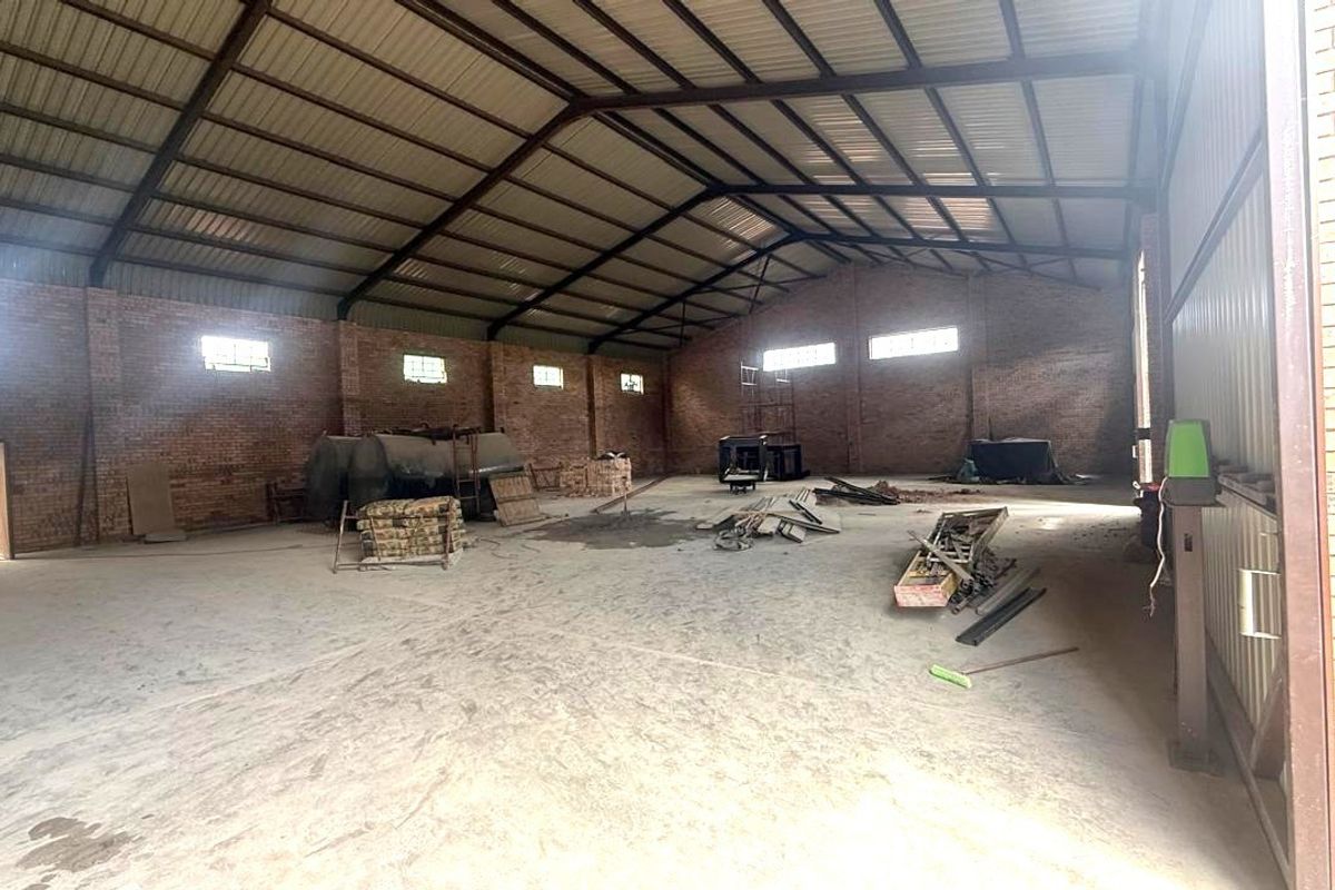 Spacious industrial utility space featuring exposed brick walls, concrete flooring, and high-clearance steel roof trusses, suitable for storage or workshop operations.