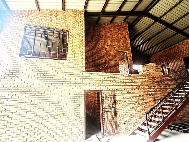 Spacious industrial utility area featuring exposed brickwork, a steel staircase, and high vaulted ceilings, currently in an unfinished state.