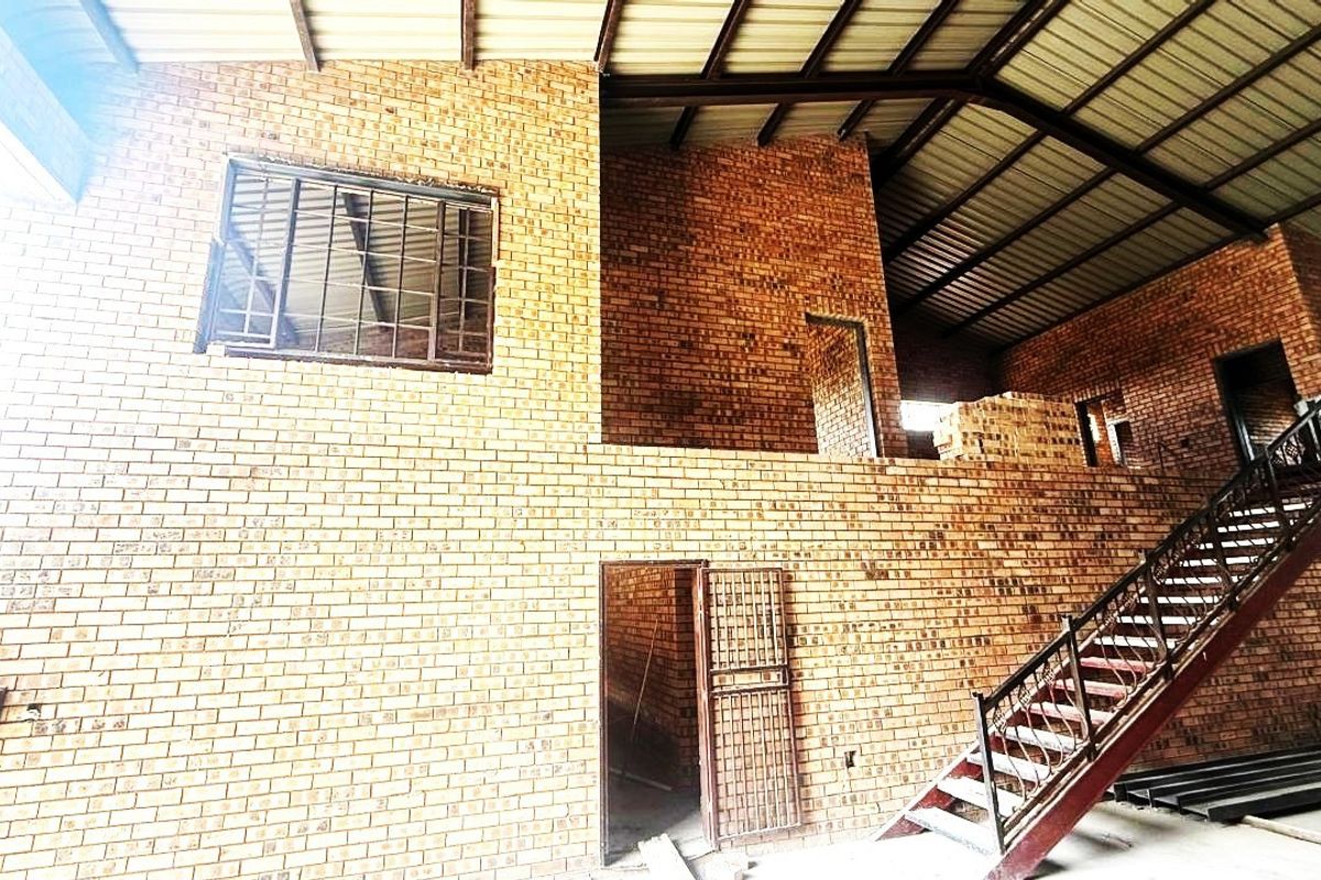 Spacious industrial utility area featuring exposed brickwork, a steel staircase, and high vaulted ceilings, currently in an unfinished state.