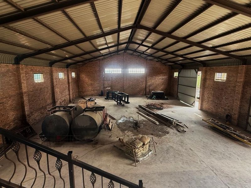 Spacious industrial utility area featuring exposed brick walls, high corrugated metal roofing with steel trusses, and durable concrete flooring.