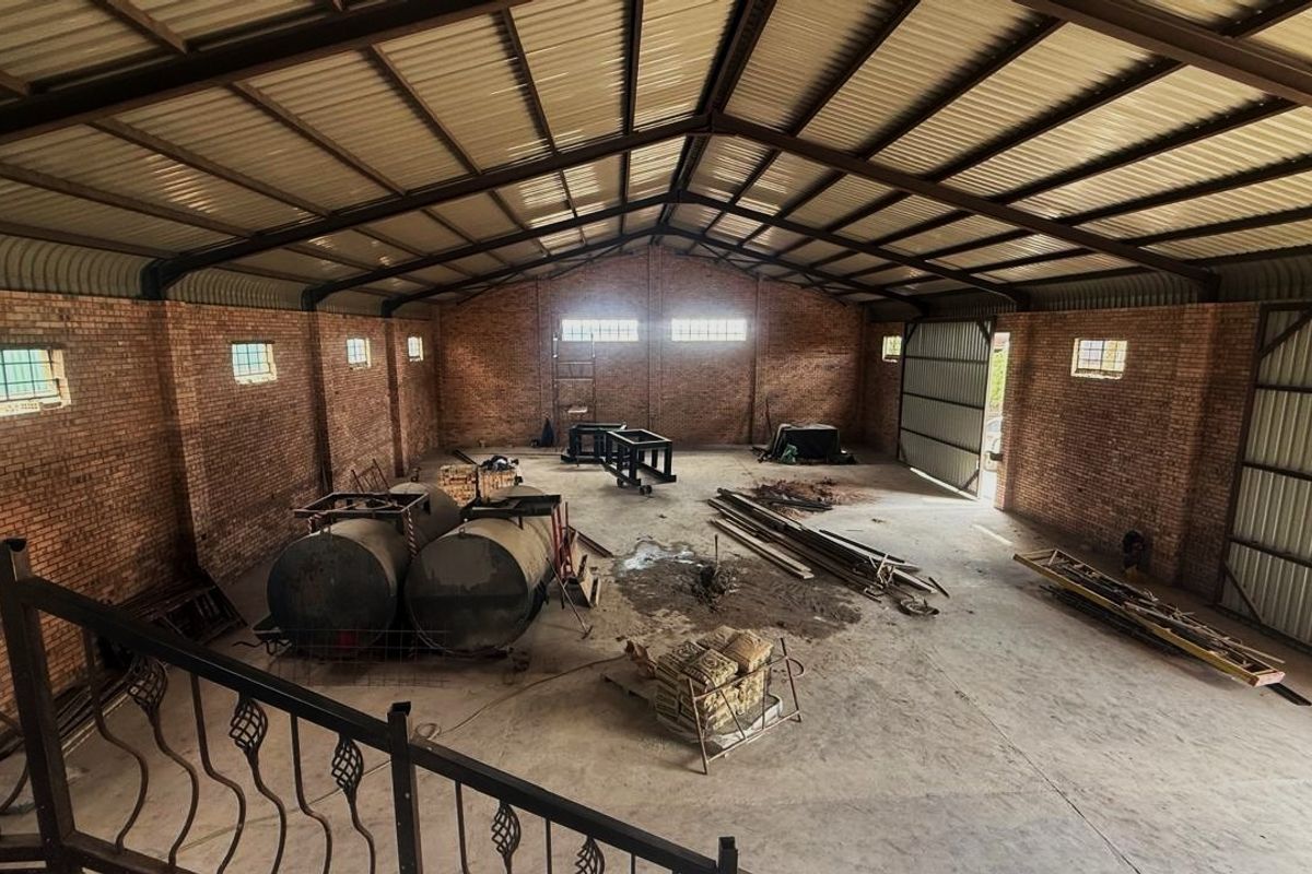 Spacious industrial utility area featuring exposed brick walls, high corrugated metal roofing with steel trusses, and durable concrete flooring.