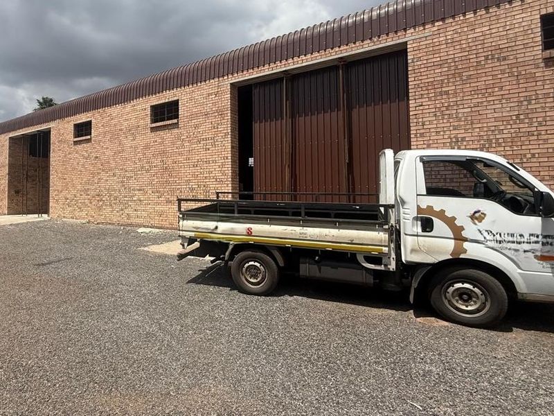 Industrial warehouse exterior featuring a face brick facade, large sliding metal doors, and a gravel yard area.