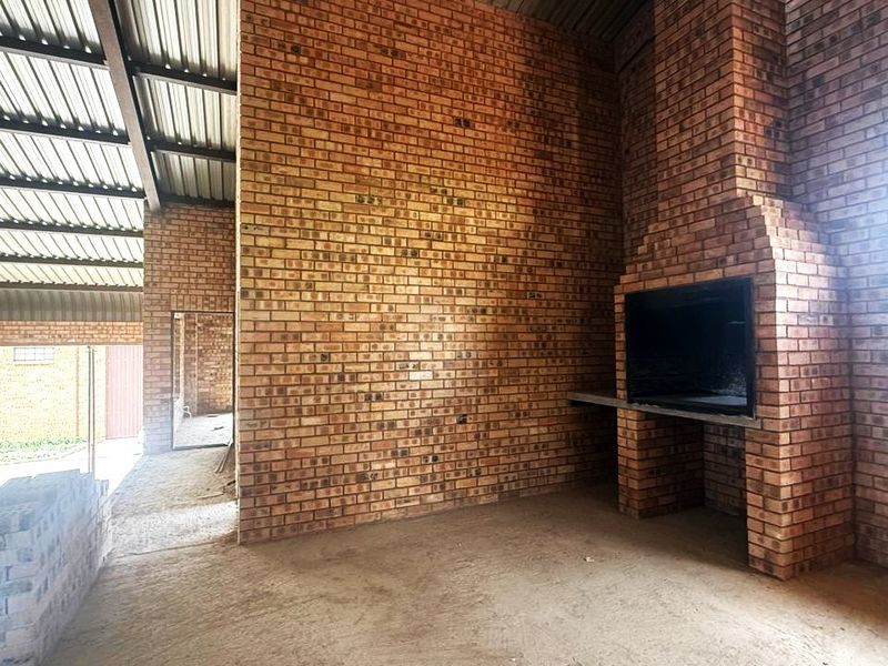 An unfinished industrial-style covered patio area featuring exposed brickwork, a built-in braai, and a corrugated metal roof structure.
