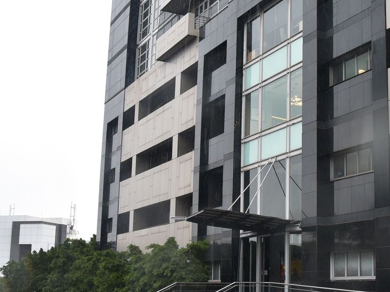 A modern commercial building facade featuring dark stone cladding, extensive glass curtain walling, and a prominent metal entrance canopy.
